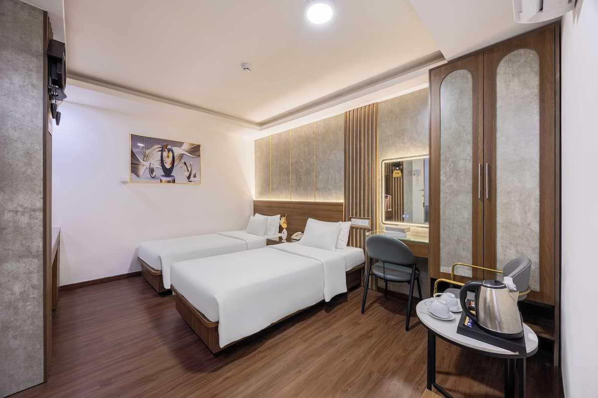 Ein Hotelzimmer mit zwei Betten, einem Schreibtisch mit Stuhl, einer Kaffeemaschine und einem großen Spiegel.