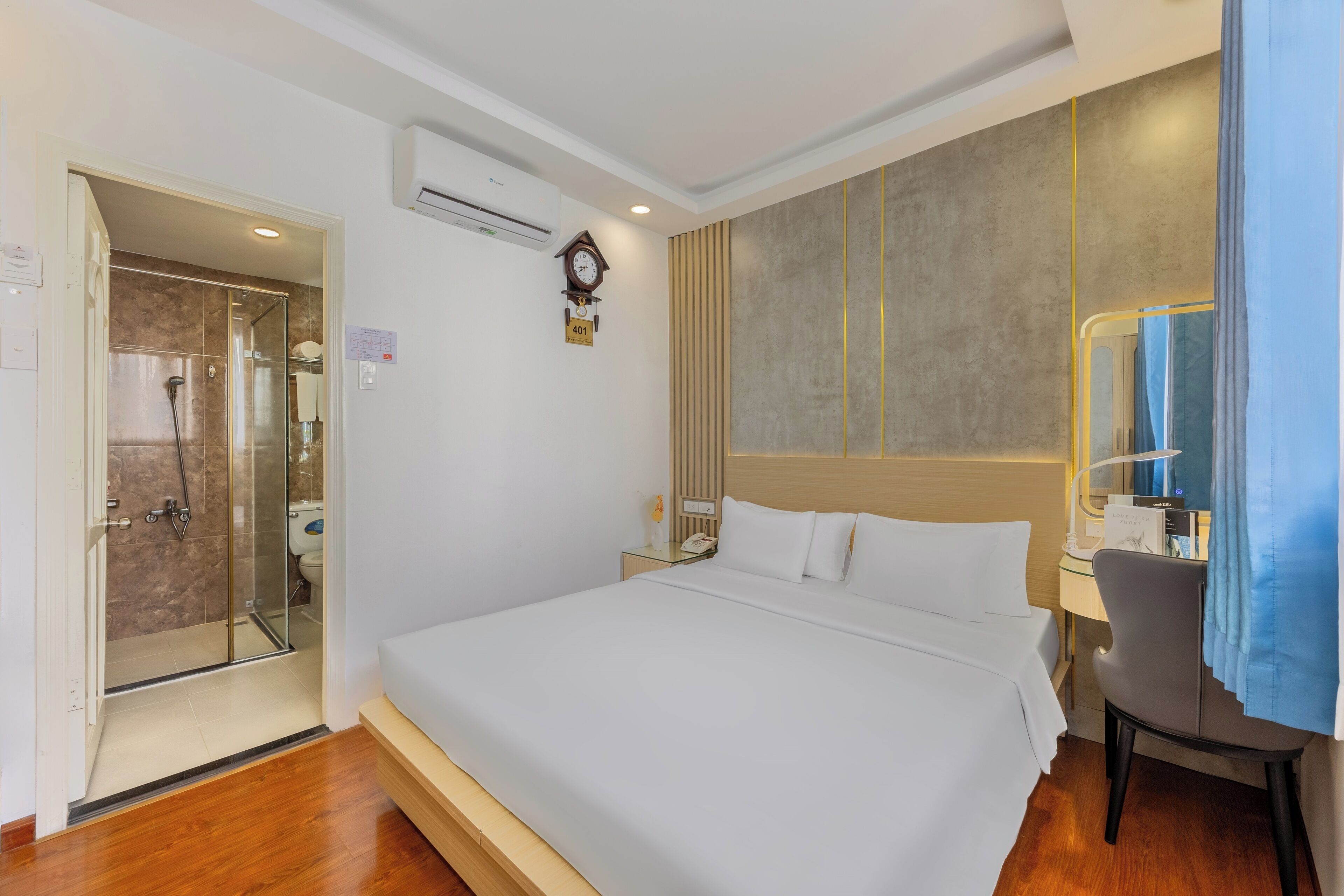 Une chambre d’hôtel avec un grand lit, un bureau avec une chaise, un espace douche et une horloge au mur.