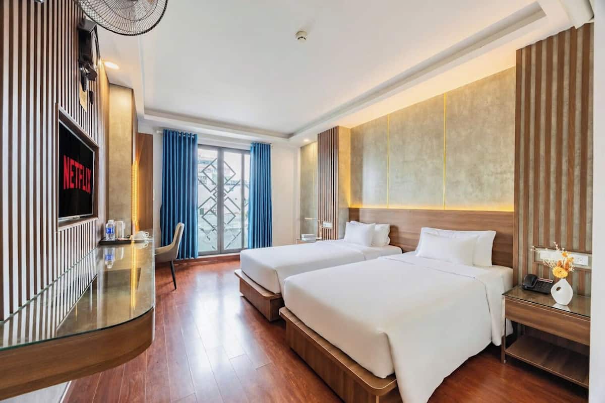 Ein Hotelzimmer mit zwei Betten, einem Fernseher, einem Schreibtisch und Blick auf die Stadt.