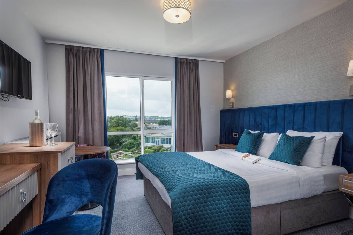 A hotel room with a large bed, a desk, a chair, and a view of the city through the window.