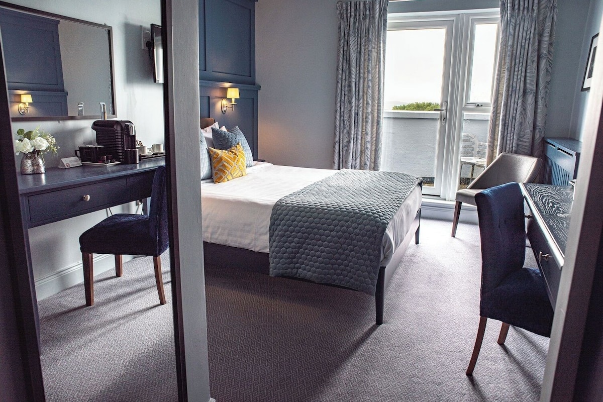 A hotel room with a bed, desk, chair, and a view of the outdoors.