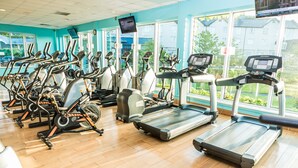 Une salle de sport équipée de divers appareils de cardio, dotée de grandes fenêtres et d’un écran de télévision.