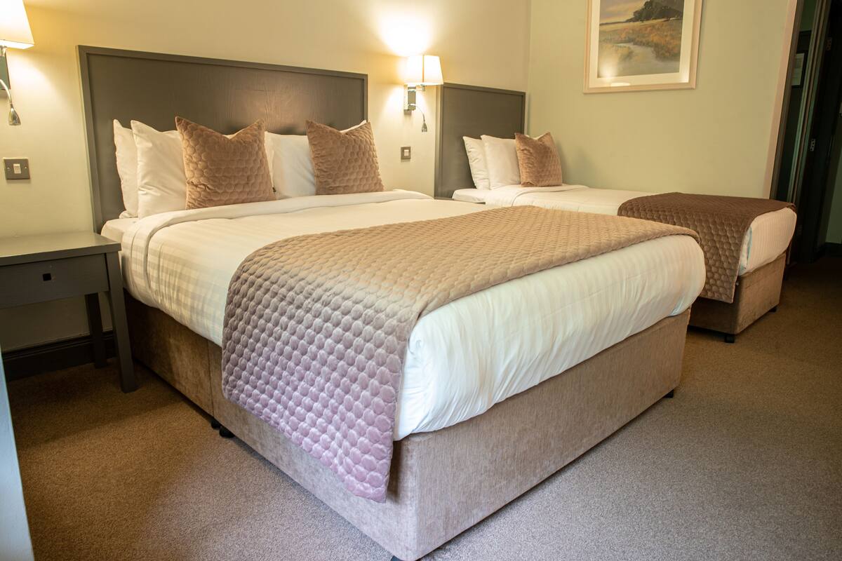A hotel room with two beds, each with a headboard, pillows, and a blanket. There are wall-mounted lamps and a painting on the wall.