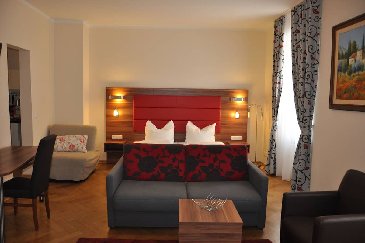 Ein modernes Hotelzimmer mit Schlafsofa, Esstisch und einem kleinen Tisch mit einer Dekoration.