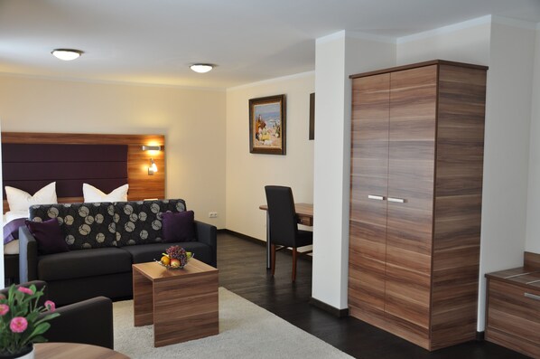 A modern hotel room with a sofa, a dining table, and a wardrobe. - BATU Apart Hotel (Munich)