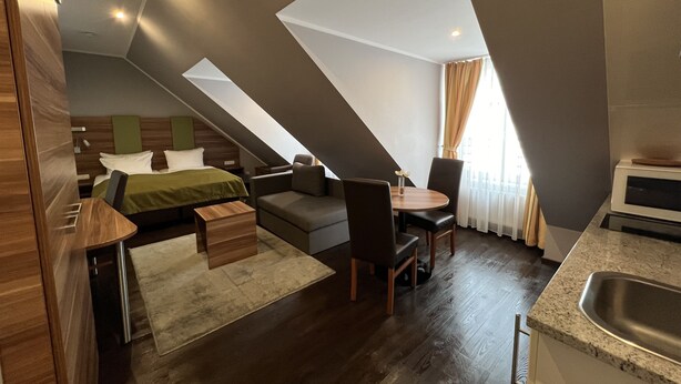 A modern hotel room with a loft bed, a sofa, a dining table, and a kitchen area. - BATU Apart Hotel (Munich)