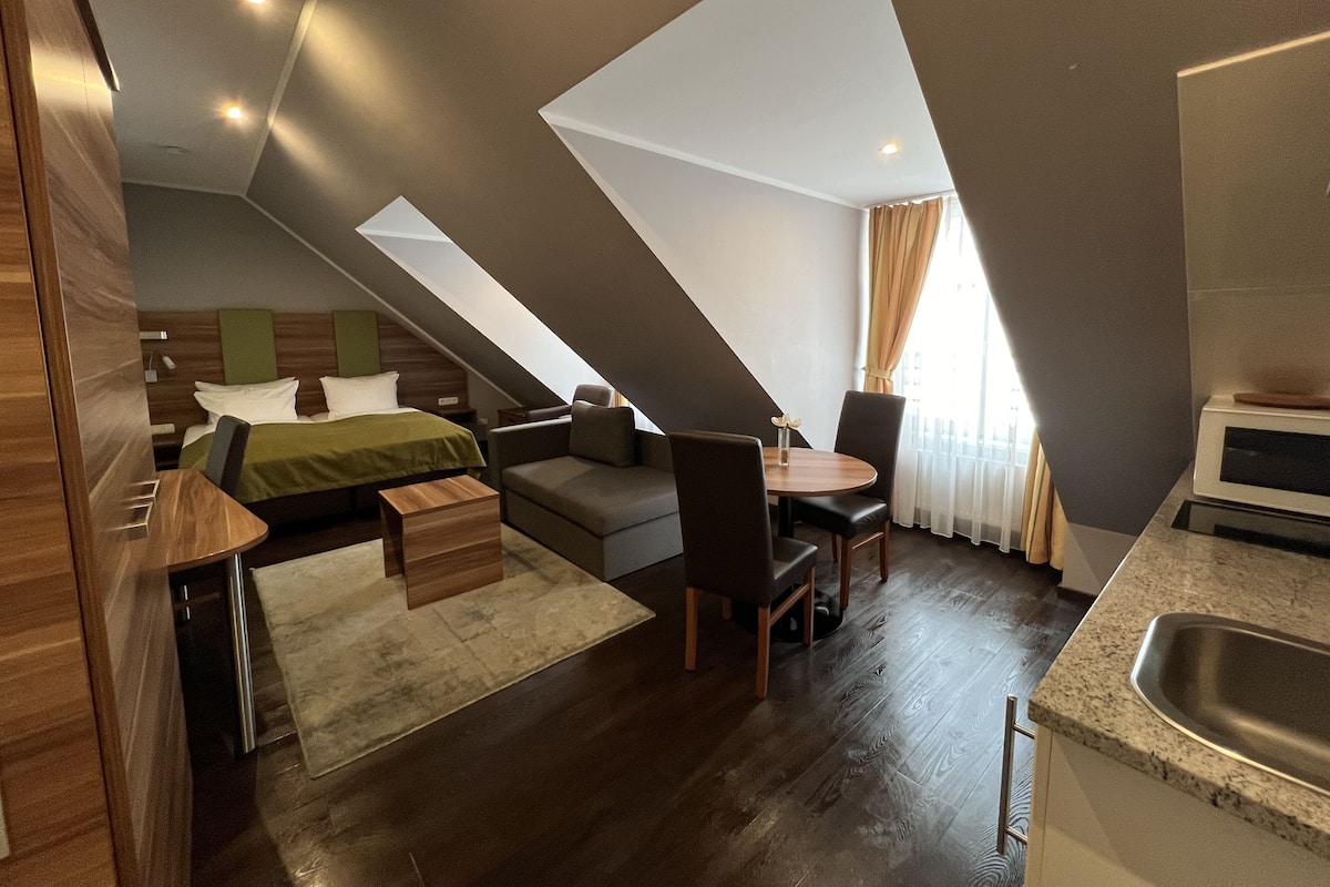 Ein modernes Hotelzimmer mit Schlafpodest, einer Couch, einem Esstisch und einer Küchenzeile.