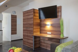 Una sala moderna con un televisor de pantalla plana montado en una pared de madera, una mesita con frutas y un sofá con un cojín verde.