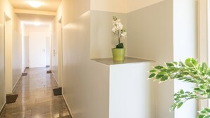 A hallway with a potted orchid and a small plant on a ledge, leading to a door at the end. - BATU Apart Hotel (Munich)