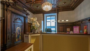 A reception area with a wooden counter, a chandelier, a window with natural light, and a decorative wall panel. - BATU Apart Hotel (Munich)