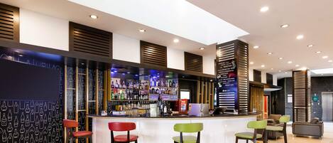 A bar area with a counter, stools, and a wall with a pattern of bottles.