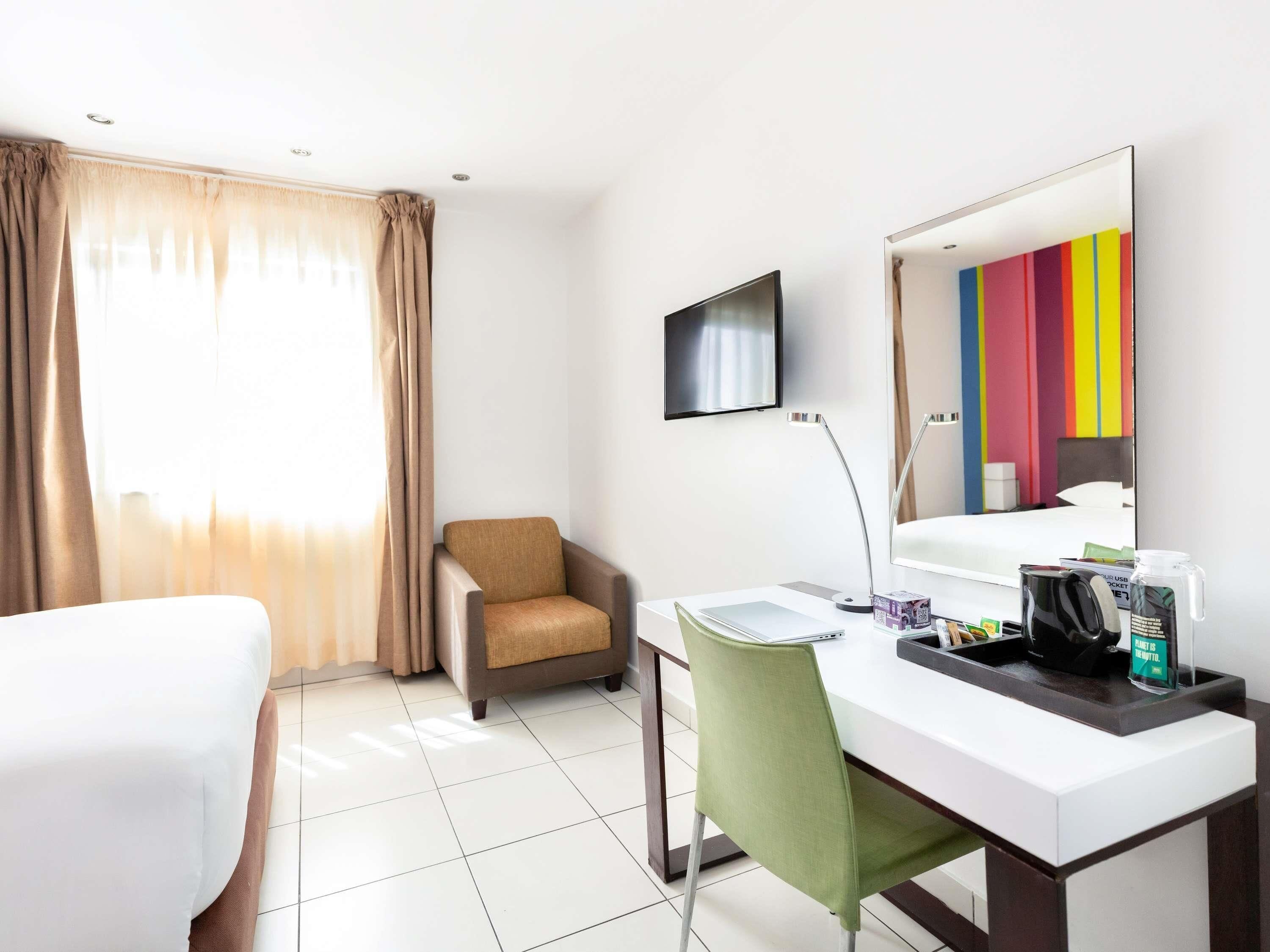 Ein Hotelzimmer mit Bett, Schreibtisch mit Stuhl, Fernseher, Spiegel und einem Fenster mit Vorhängen.