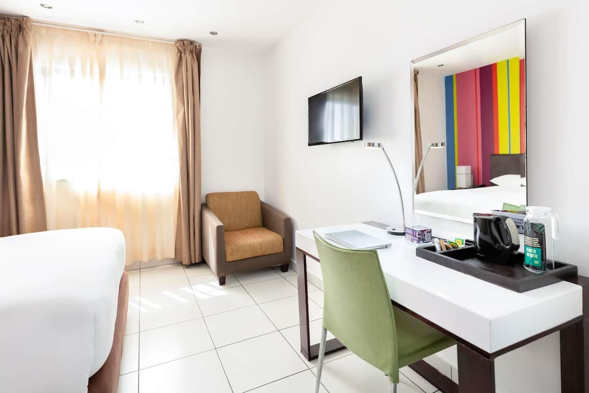 Ein Hotelzimmer mit Bett, Schreibtisch mit Stuhl, Fernseher, Spiegel und einem Fenster mit Vorhängen.