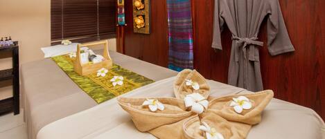 Habitación de hotel con dos camas, un armario de madera, una bata, y una bandeja con toallas y flores.