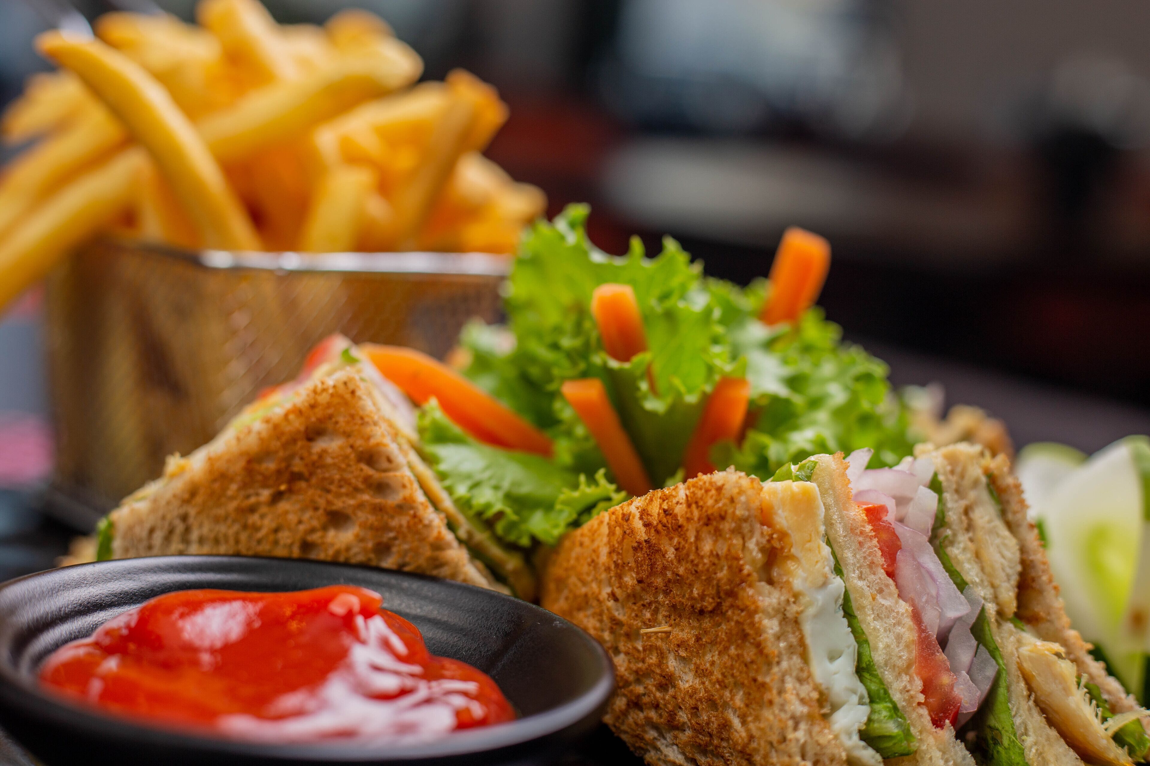 A sandwich with lettuce, tomato, and other vegetables, a side of fries, and a small bowl of ketchup.
