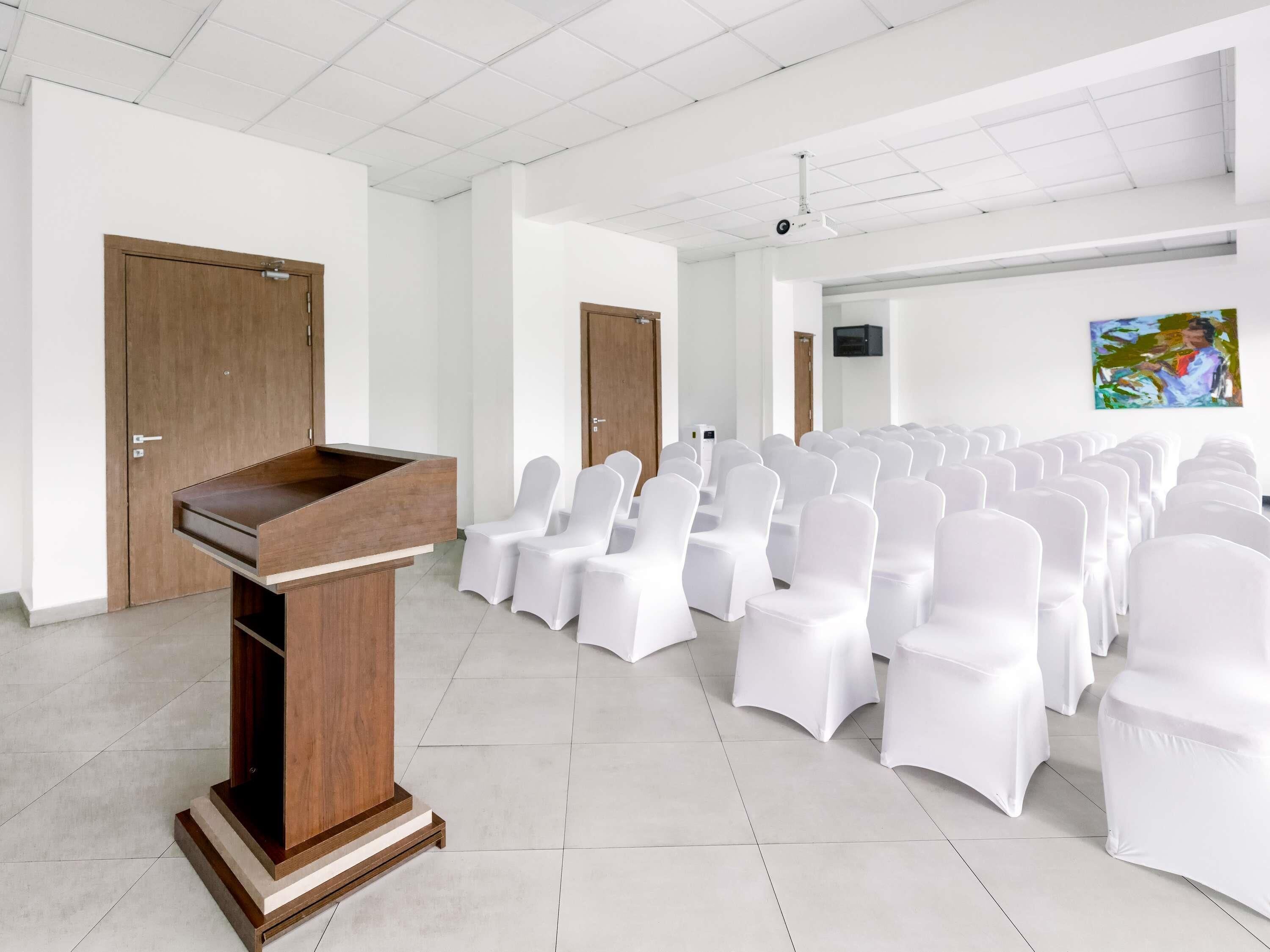 A conference room with a wooden podium, white chairs, and a projector screen.