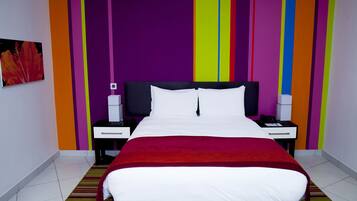 Une chambre d’hôtel moderne avec un grand lit, deux tables de chevet et un mur rayé aux couleurs vives.