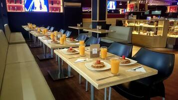 A breakfast buffet with tables set with plates of pancakes, orange juice, and a small fruit garnish.