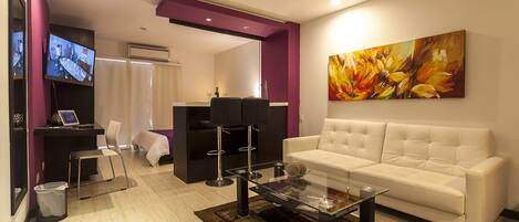 A modern living room with a white sofa, a glass coffee table, a flat-screen TV, and a large floral painting on the wall.