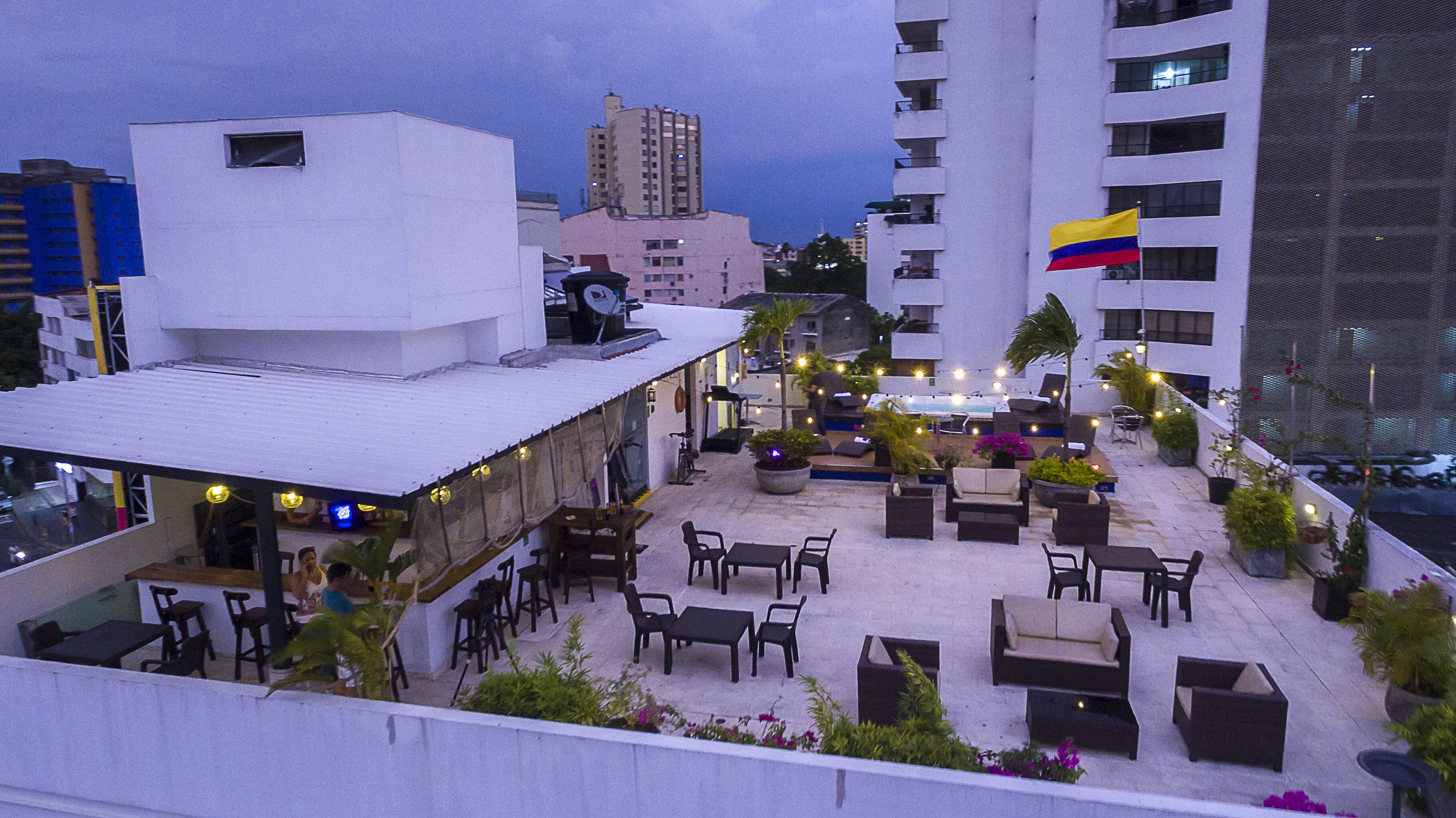 Un espacio al aire libre con patio, mobiliario, piscina, edificios circundantes y una bandera.