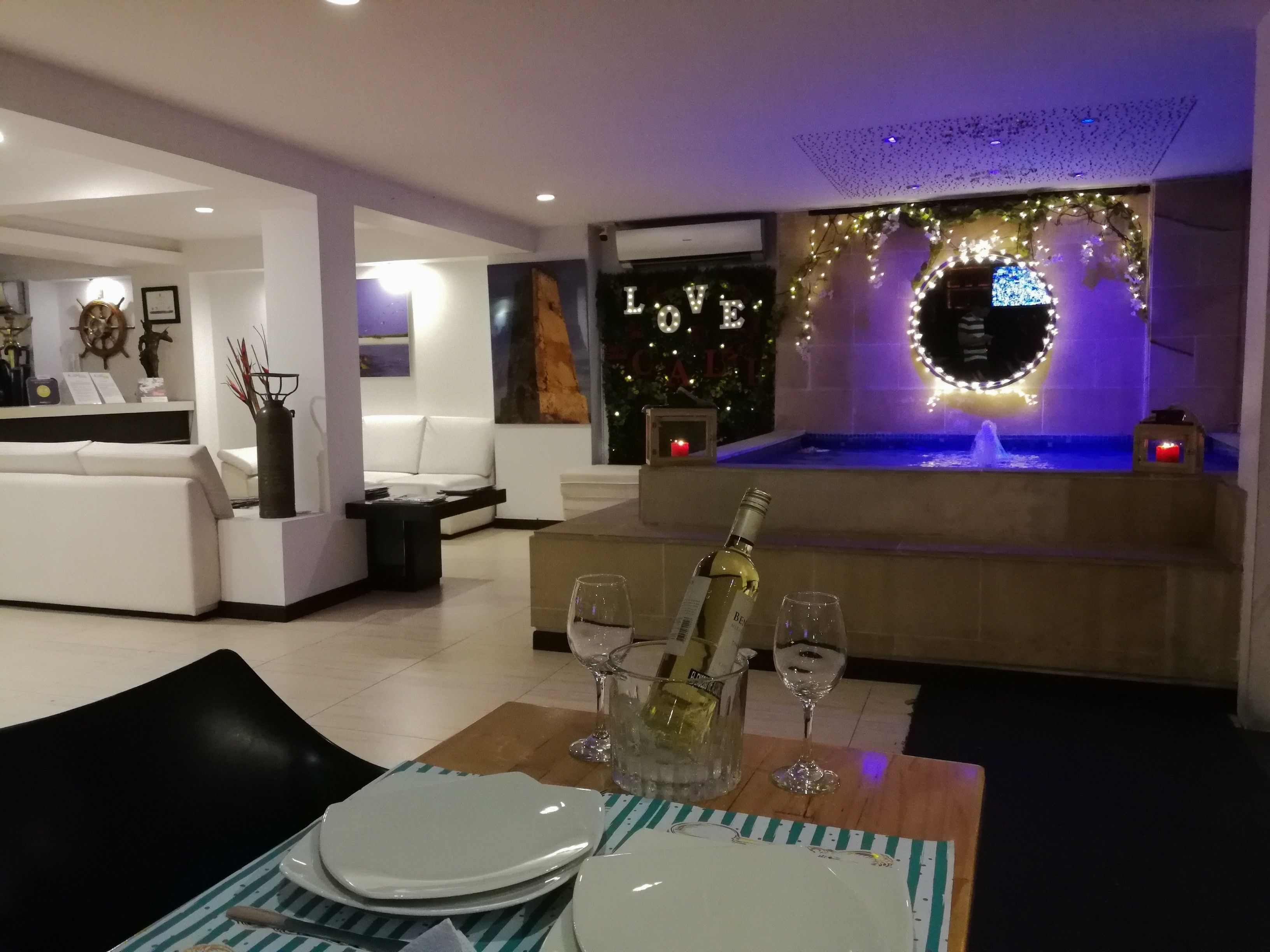 A modern living room with a fireplace, a seating area, and a dining setup with a bottle of champagne and glasses.