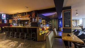 A bar area with a wooden counter, multiple shelves with bottles, and a chalkboard menu listing beverages and food items. - Aqua Granada Hotel (Cali)