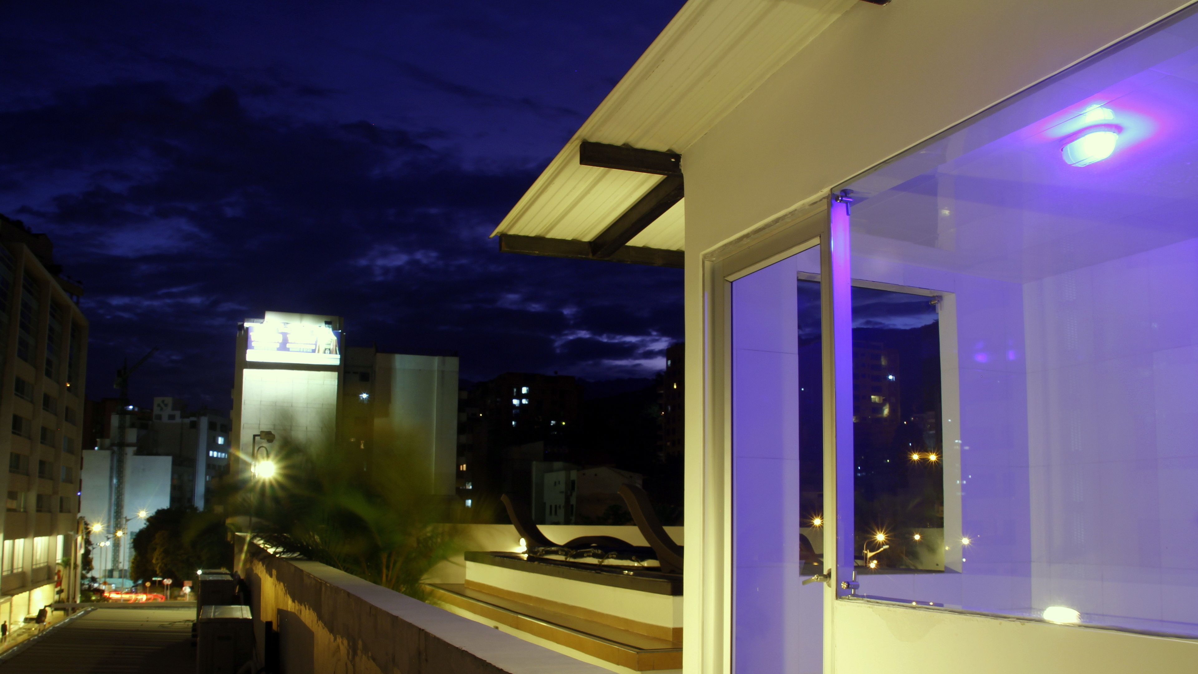 A modern building with a glass facade, a balcony, and a view of the cityscape at night.