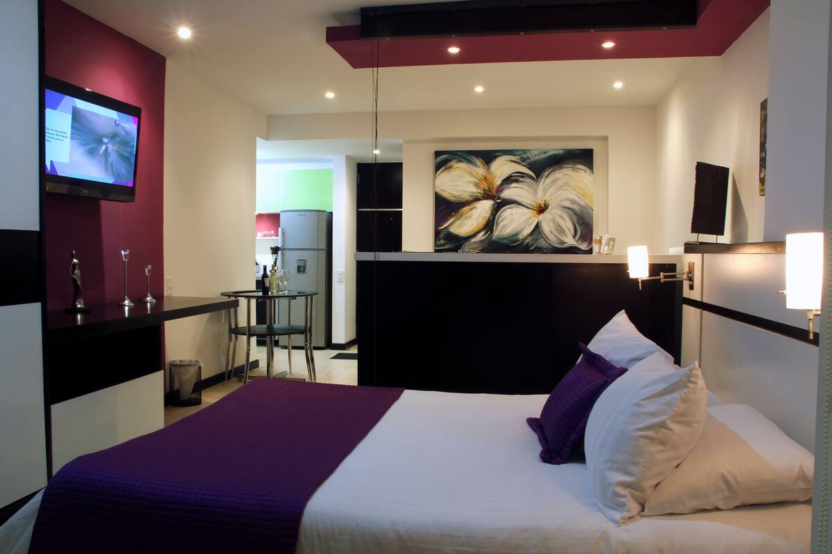 Habitación de hotel con cama, escritorio, silla, televisor y un cuadro en la pared.