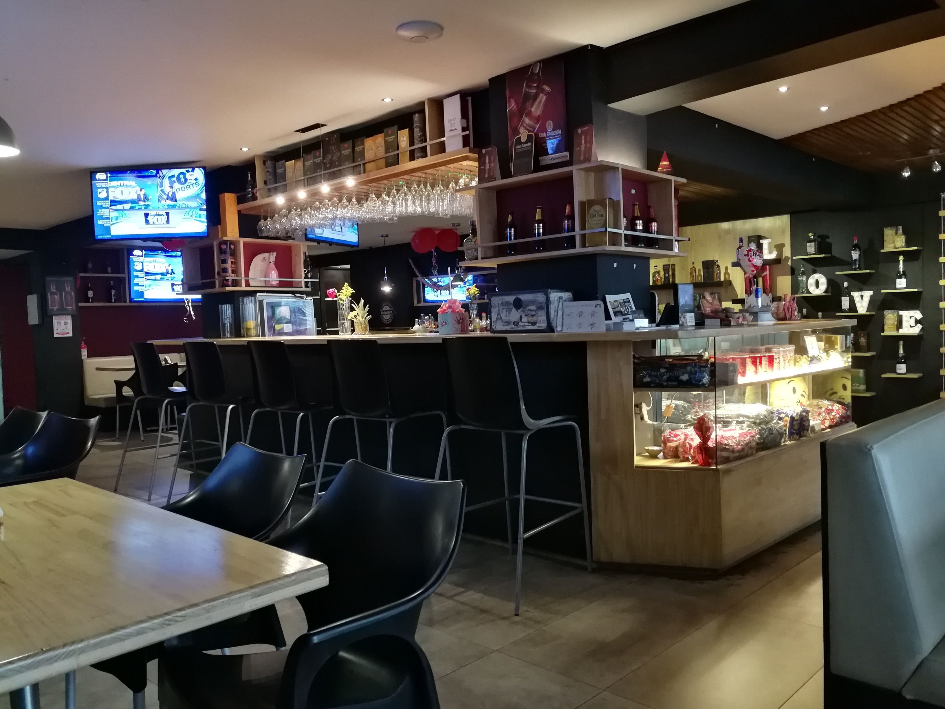 A bar area with multiple seating options, including bar stools and tables, and a display of various bottles and glasses.