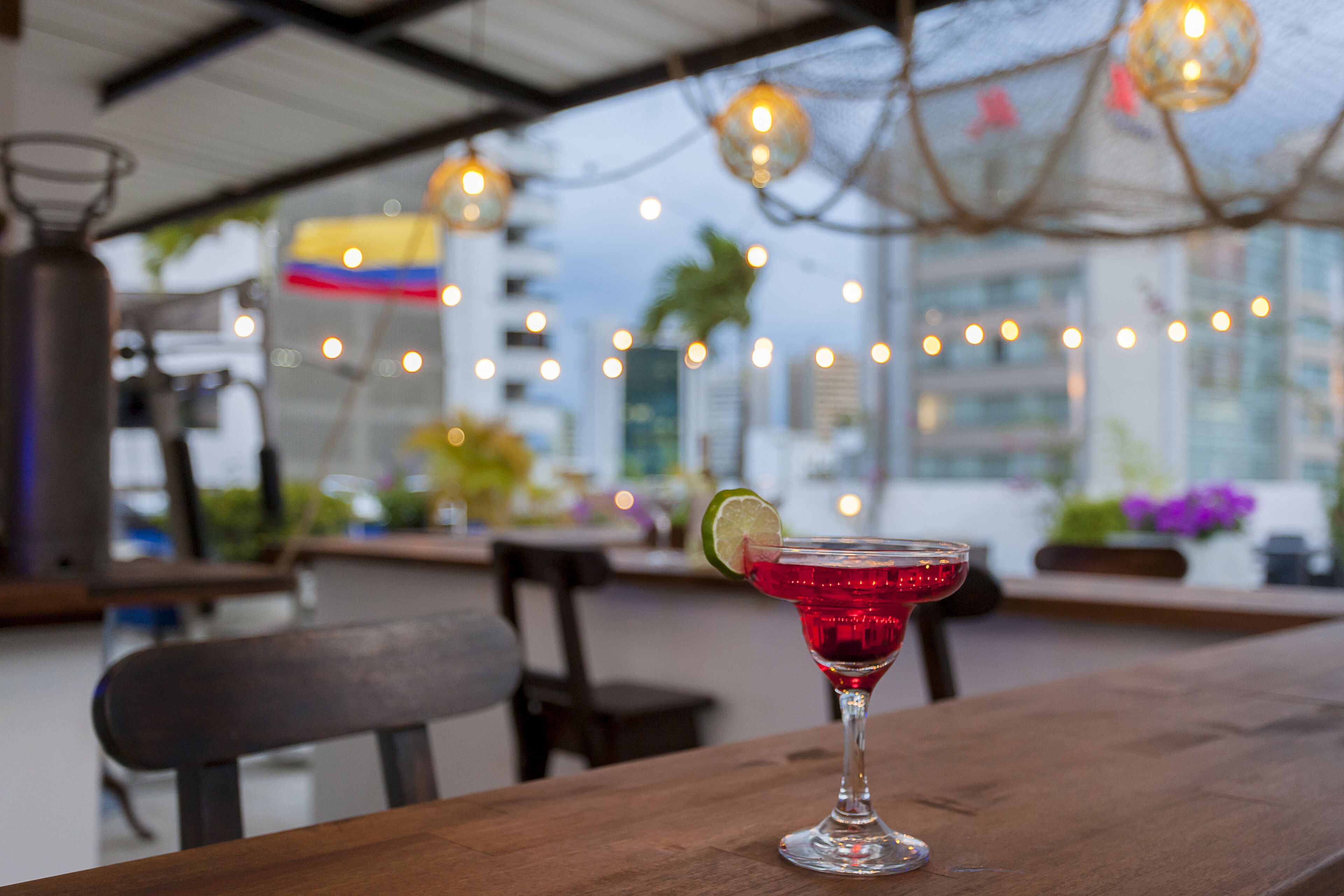 A cocktail on a wooden table with a city view in the background.