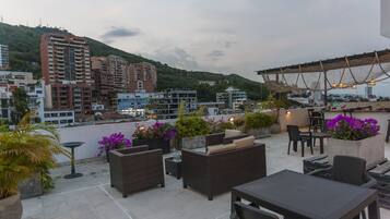 A rooftop terrace with outdoor seating, potted plants, and a view of surrounding buildings.
