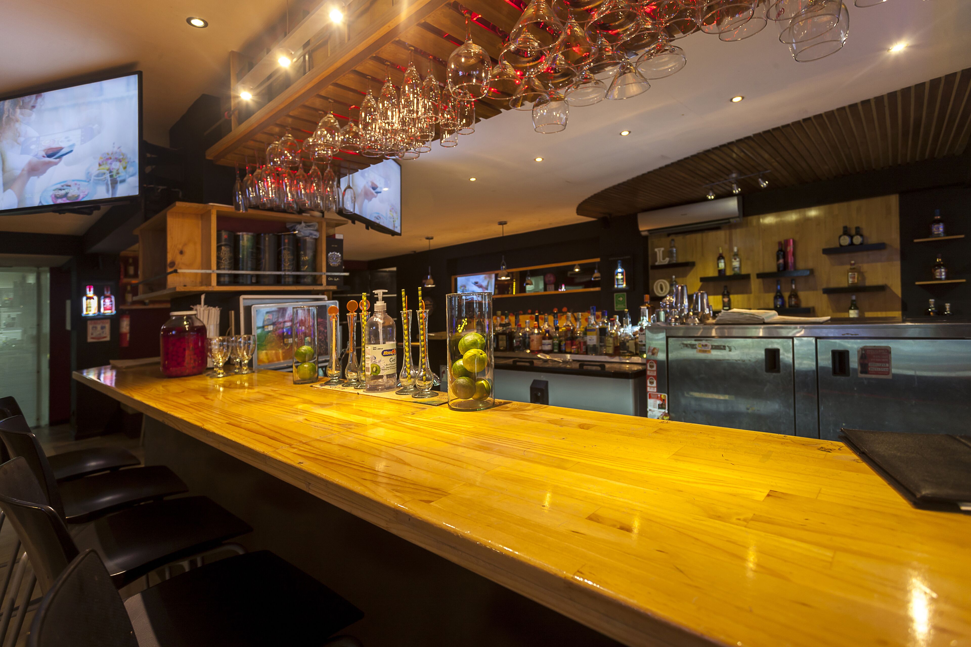 A bar area with a wooden counter, bar stools, and a television screen.