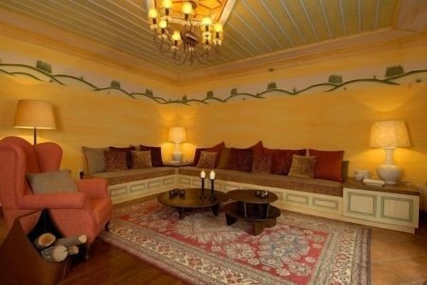 A cozy living room with a sectional sofa, two side tables with lamps, a patterned rug, and a chandelier.