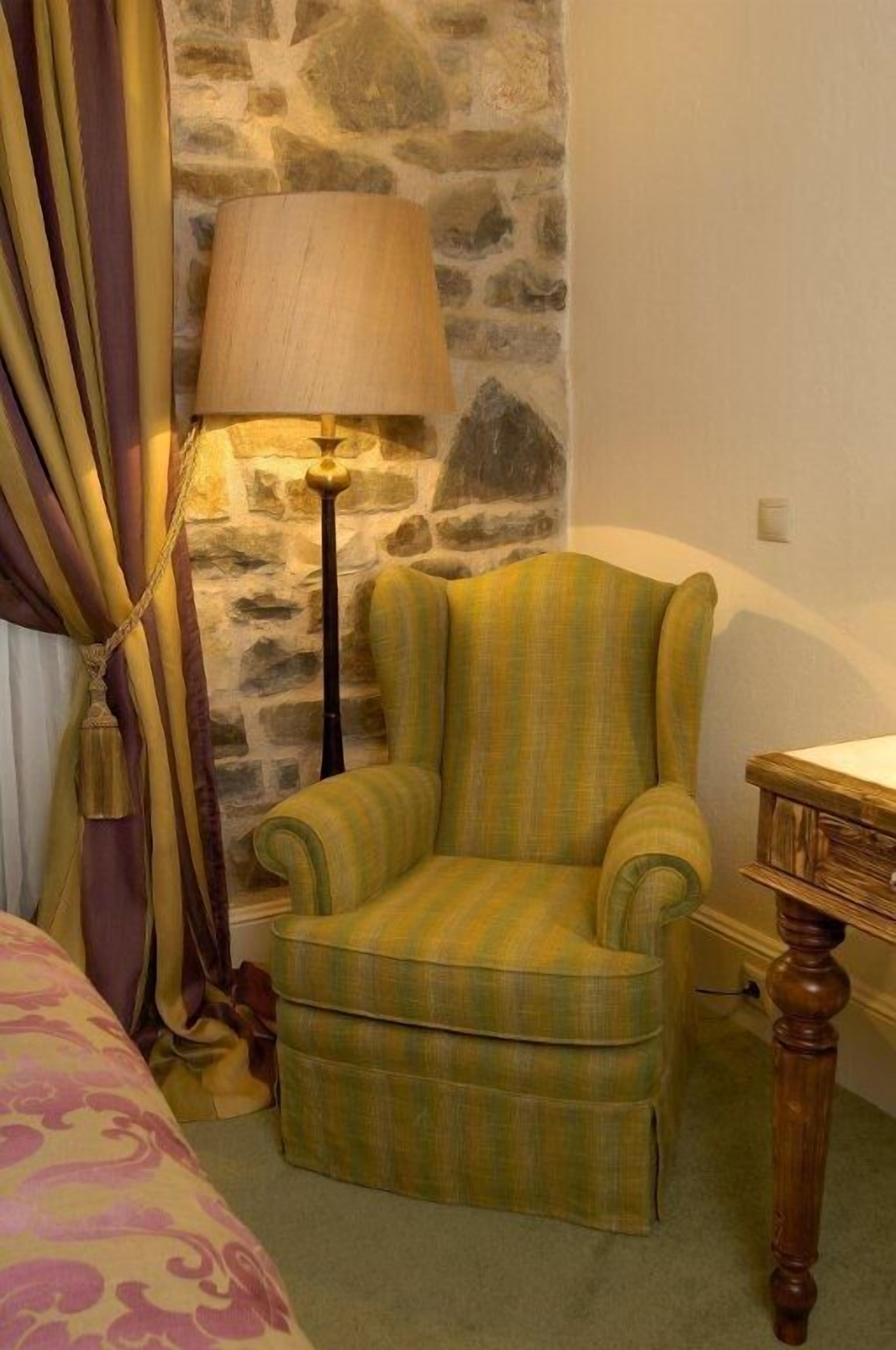 A room with a green striped armchair, a lamp, and a wooden desk.