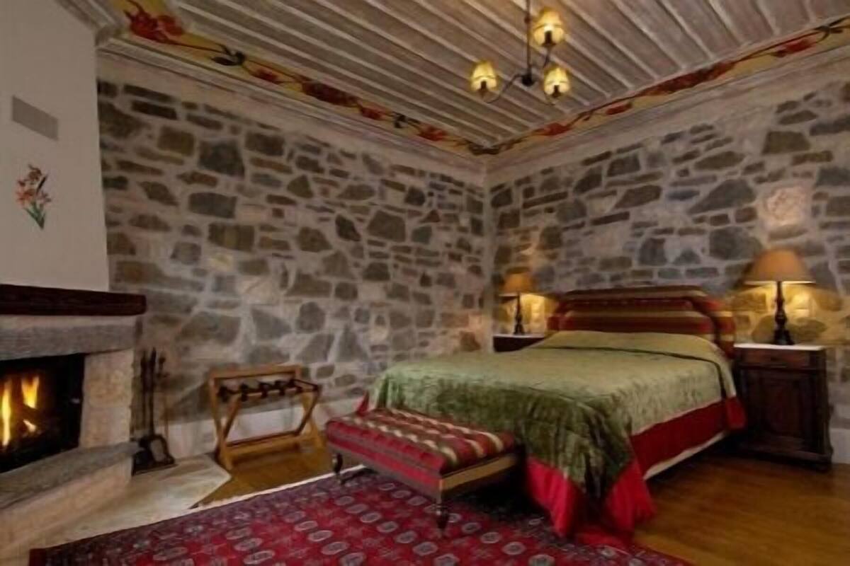 A stone-walled room with a bed, a fireplace, and a rug.