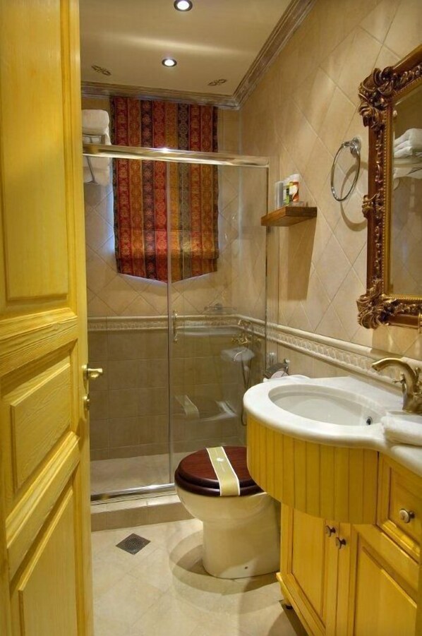 Un baño con ducha acristalada, inodoro con asiento de madera y lavabo con espejo.
