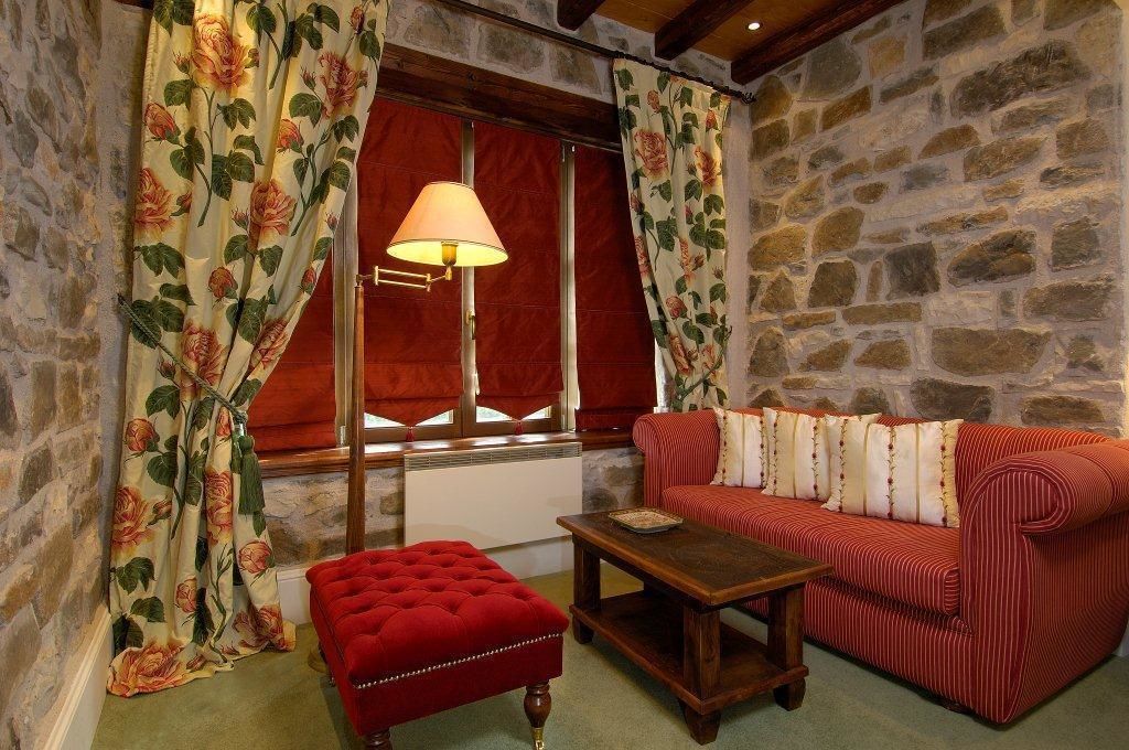 A cozy room with a stone wall, a red sofa, a red ottoman, and a table with a lamp.