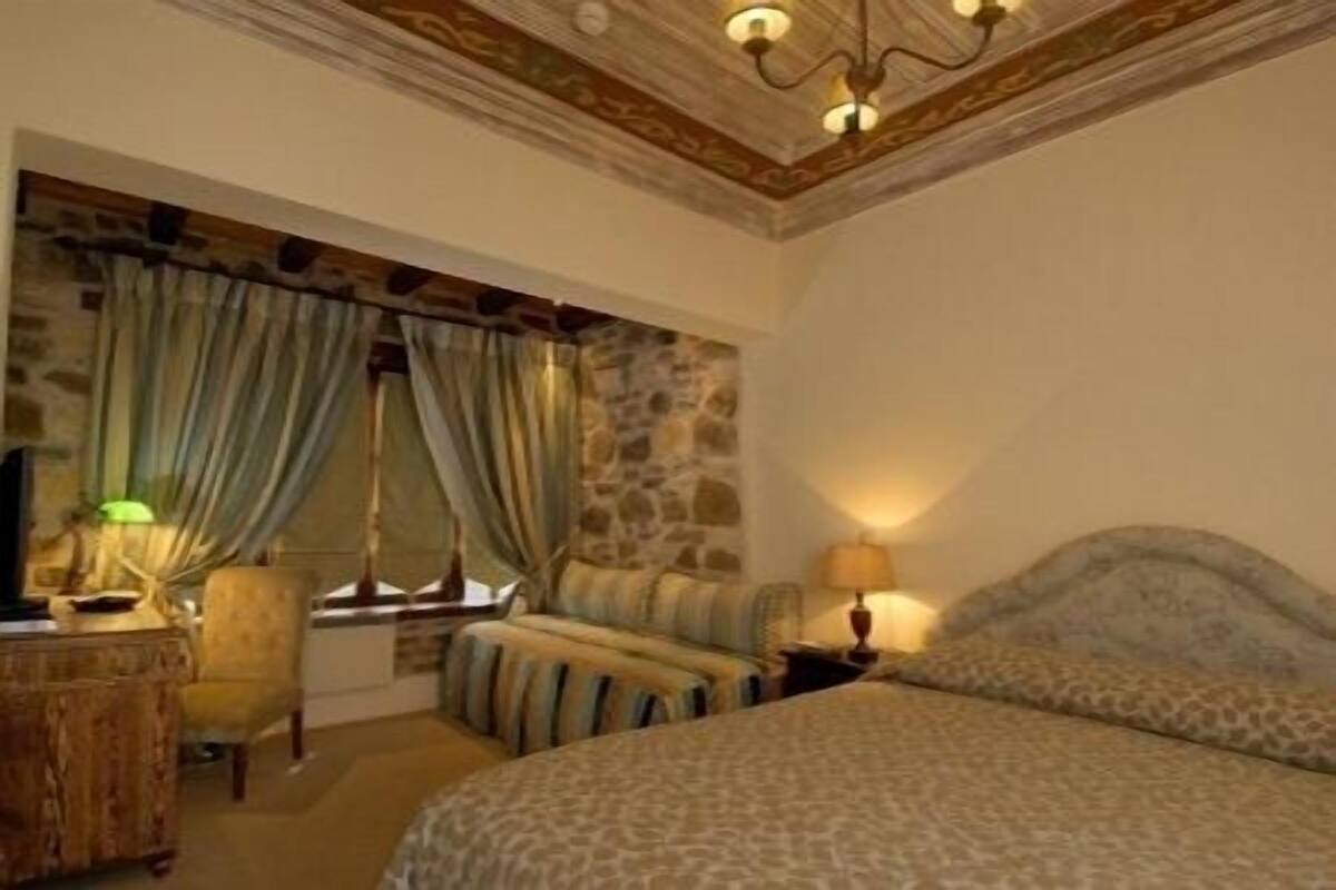 A bedroom with a bed, a desk, a chair, a lamp, and a stone wall.