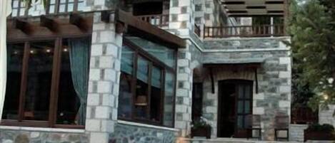 A stone building with large windows and a patio area with wooden furniture.