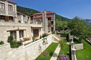 Un edificio de piedra con un patio, una escalera y vistas a una colina boscosa.