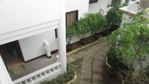 En gårdhave med plantekrukker, flisegulv og en hvid bygningsfacade.