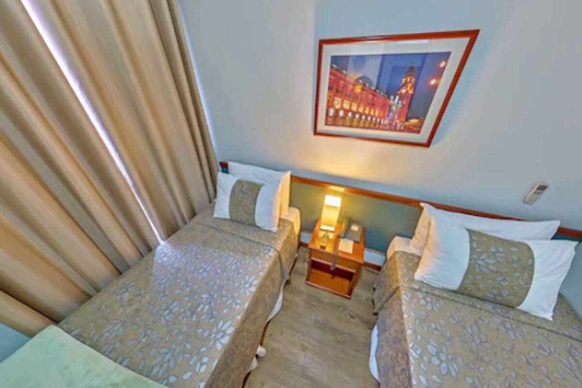 A hotel room with two beds, a nightstand with a lamp, and a framed picture on the wall.