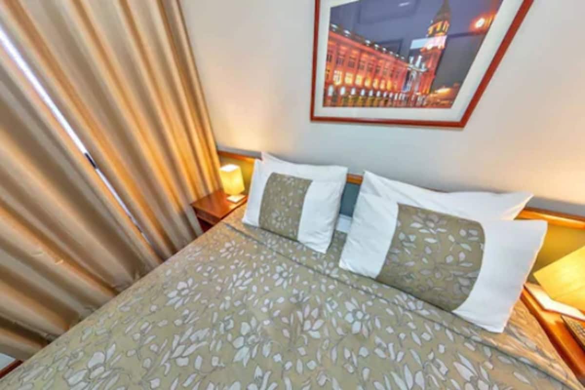 A hotel room with a bed, a nightstand with a lamp, and a framed picture on the wall.