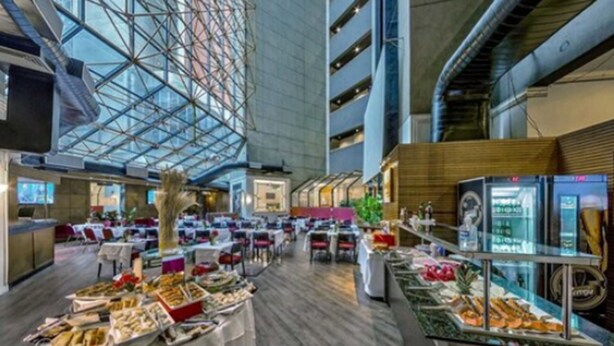 A spacious hotel lobby with a high ceiling and a glass atrium, featuring a buffet with various food items and a seating area with tables and chairs. - Hotel Massis (São Paulo)