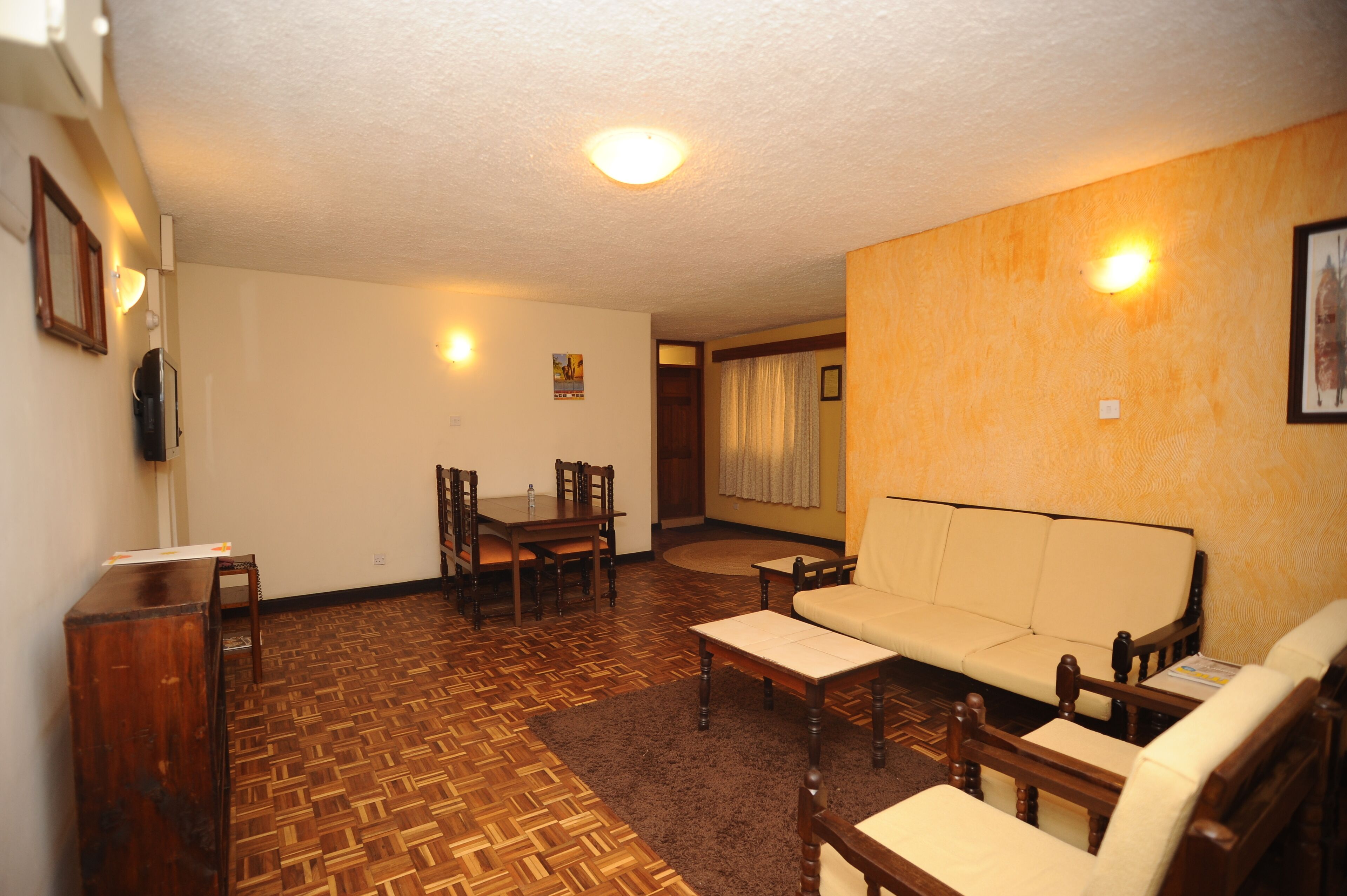 A living room with a wooden parquet floor, a sofa, a coffee table, a dining table with chairs, and a fireplace.