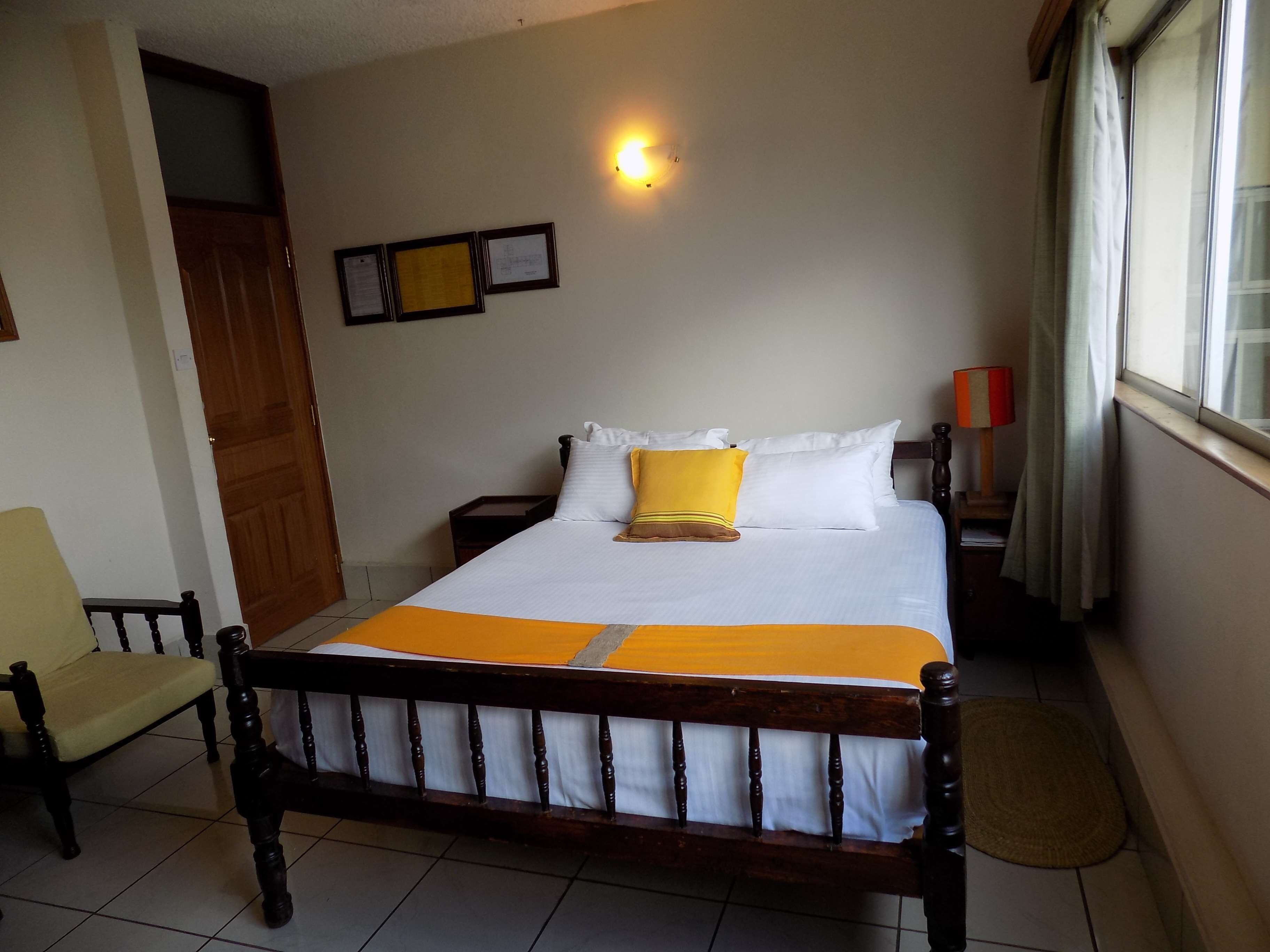 A neatly arranged bedroom with a bed, a chair, a nightstand, and a wall-mounted light fixture.