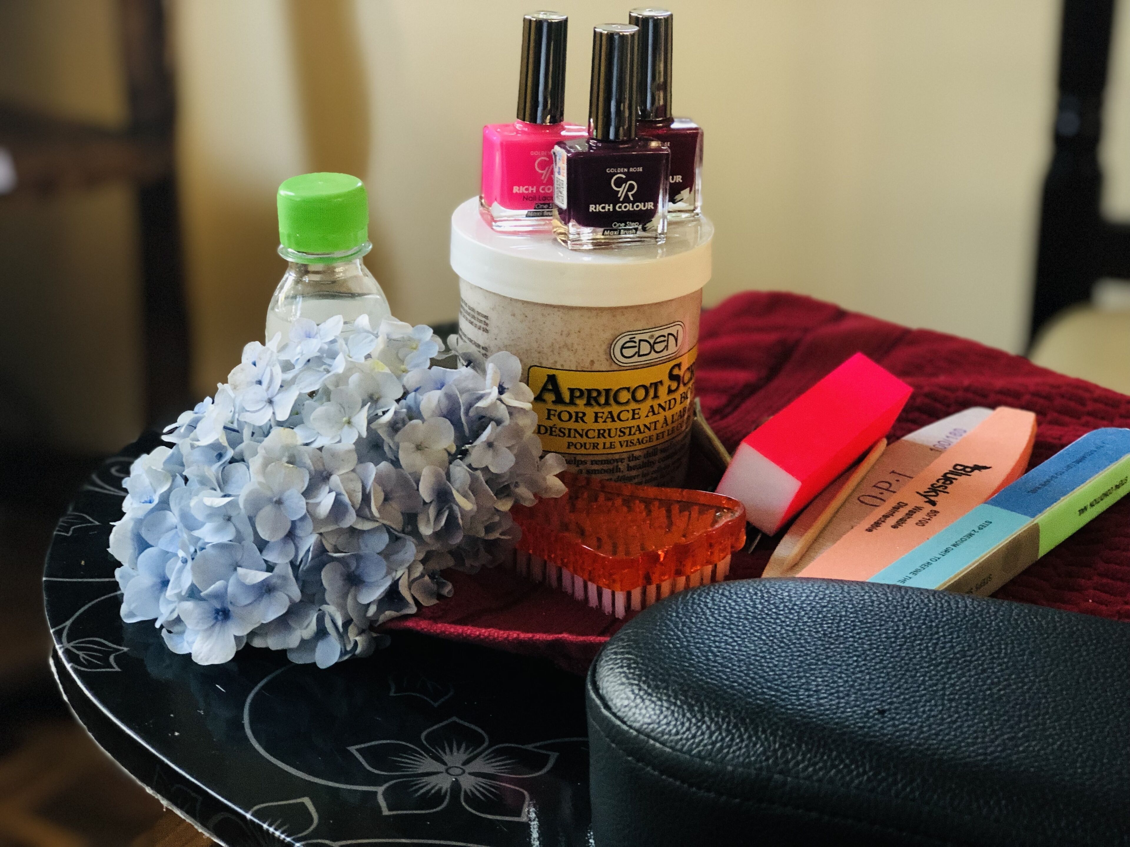 A table with various beauty products, including nail polish, a bottle of Eden apricot serum, and a glass of water.