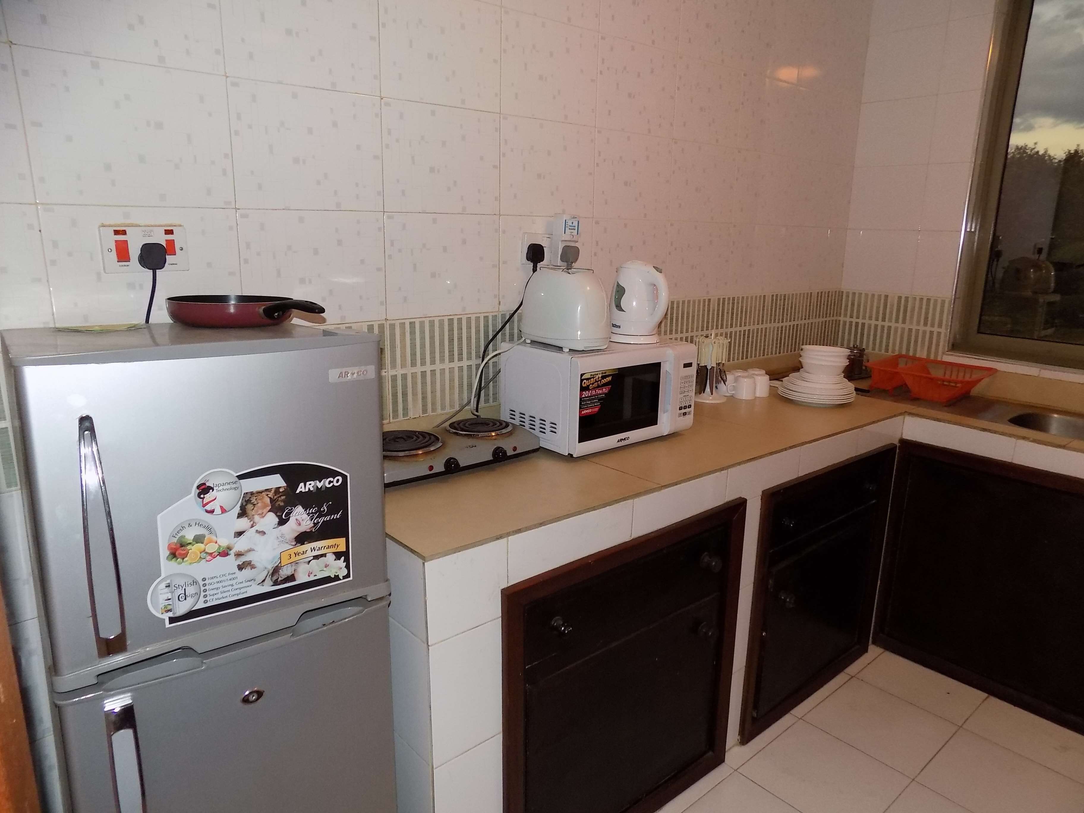 A compact kitchen with a refrigerator, microwave, and stove. There are cabinets and a window above the sink.