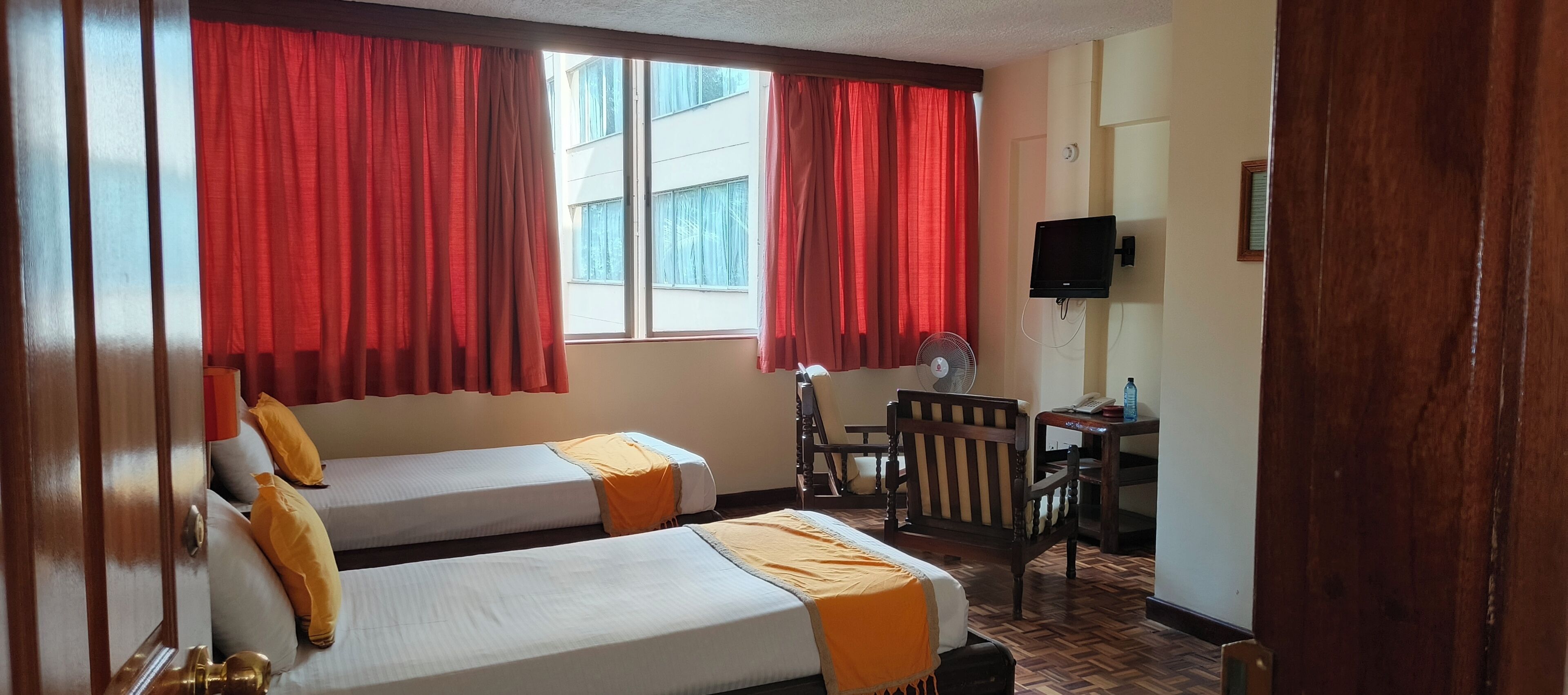 Ein Hotelzimmer mit zwei Betten, roten Vorhängen, einem Holztisch, einem Stuhl und einem Fernseher.