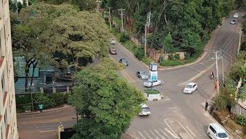 A parking area with multiple cars, a road with vehicles, and buildings in the background.